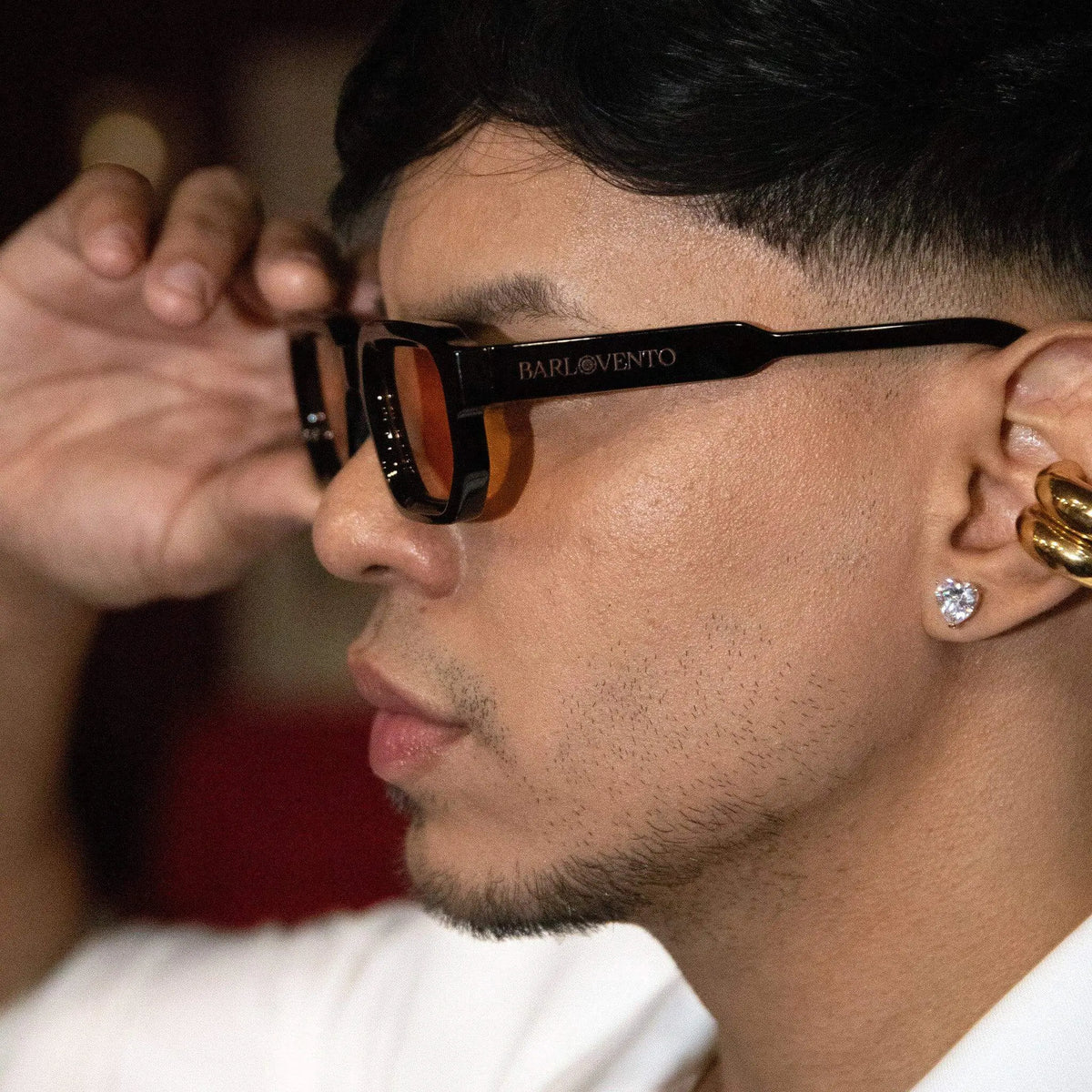 Gafas de sol negras de estilo urbano con lentes naranjas en perfil de joven con accesorios dorados.