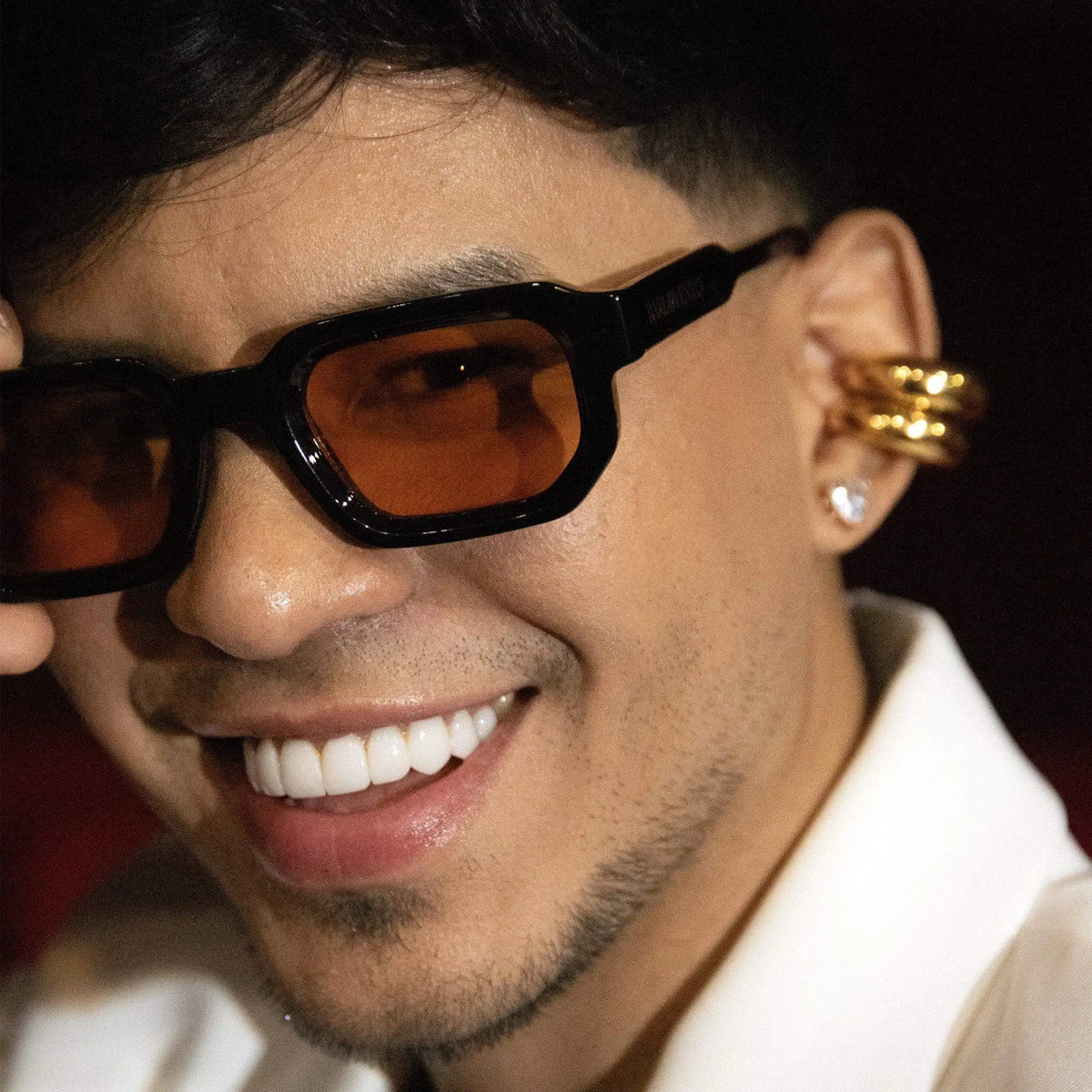 Gafas de sol negras de estilo rectangular con lentes naranjas, portadas por un hombre joven con camisa blanca.