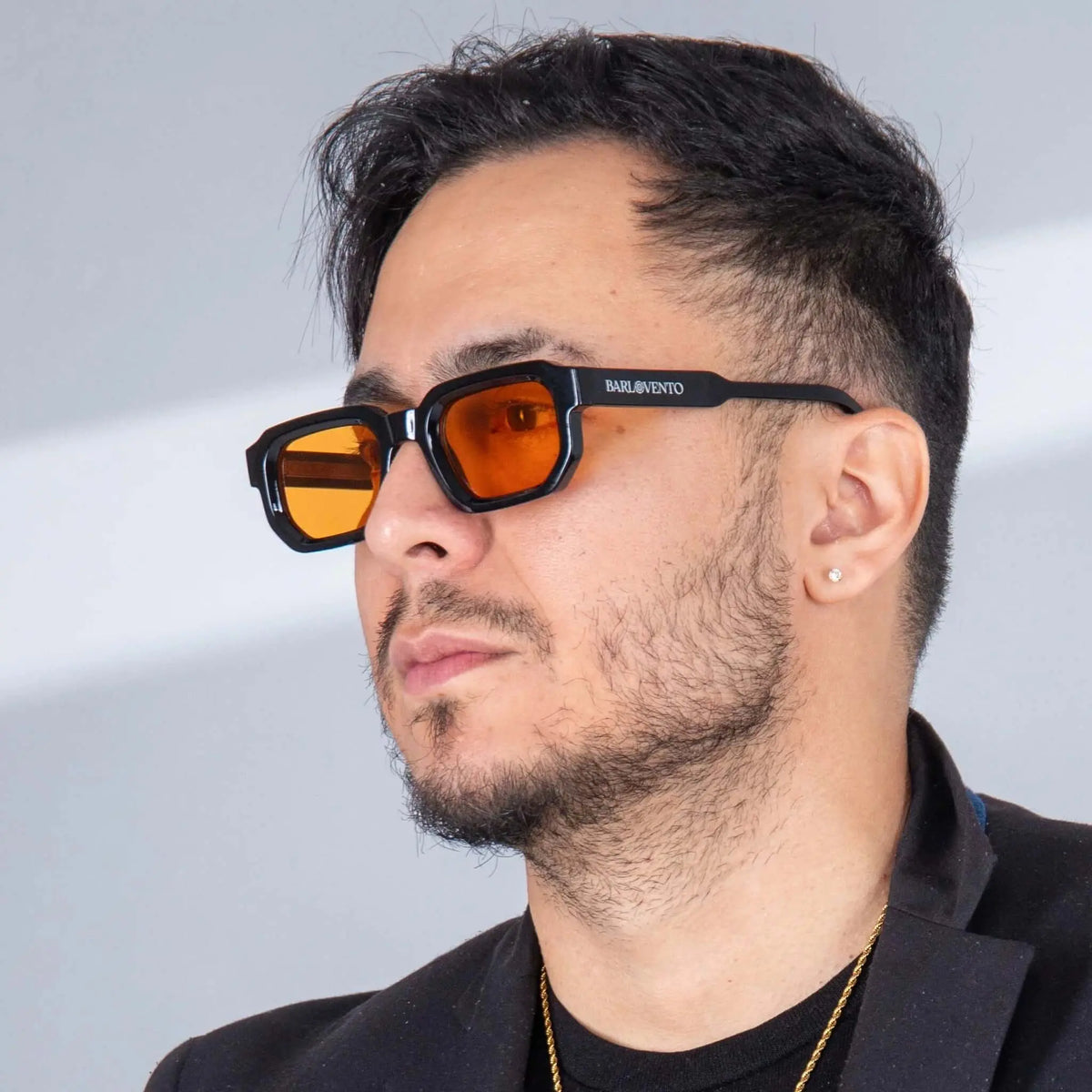 Hombre con gafas de sol negras de montura rectangular gruesa y lentes naranjas estilo moderno.