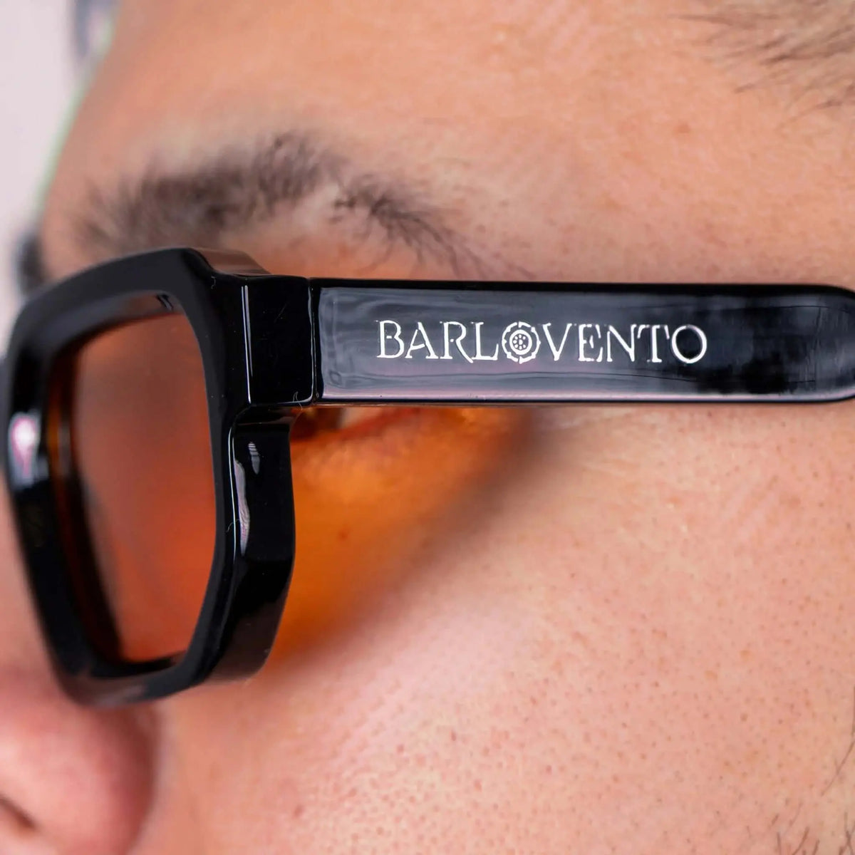 Gafas de sol negras de estilo grueso con montura geométrica y lentes naranja cálido puestas en primer plano.