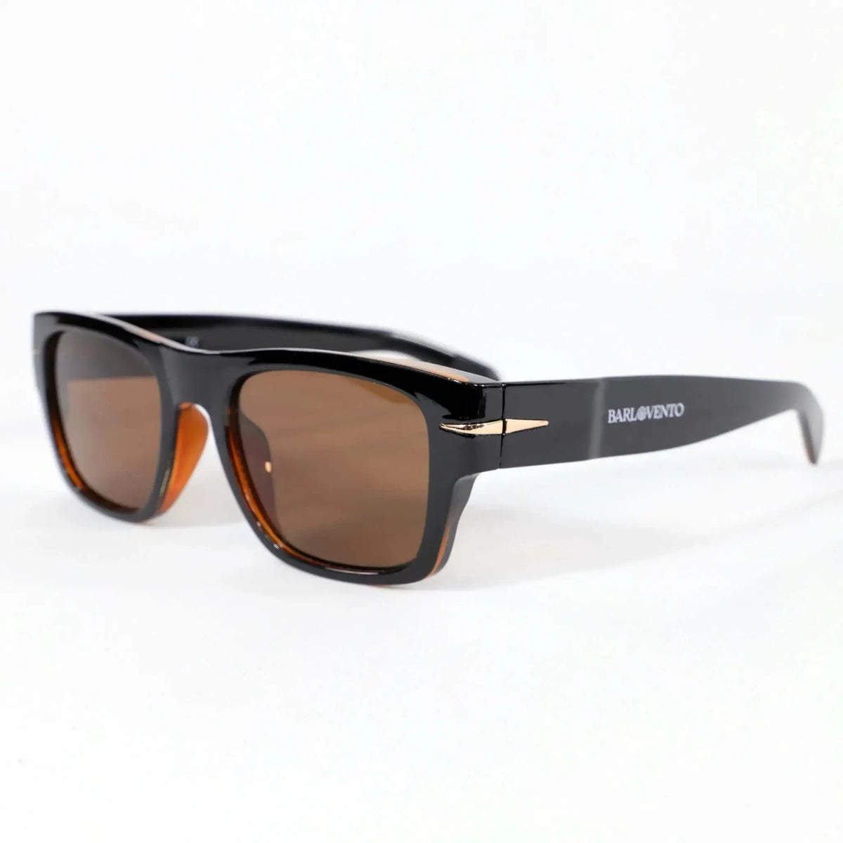 Gafas de sol retro con montura negra brillante, detalles dorados y cristales marrones sobre fondo blanco.
