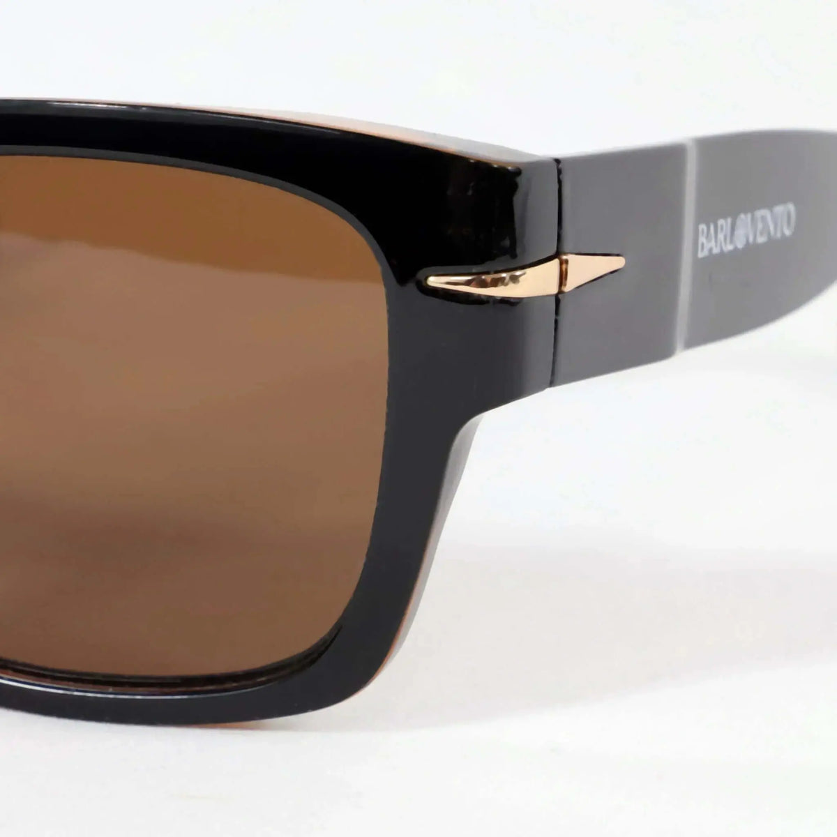 Gafas de sol retro negras con acabado brillante, lentes marrones y detalle metálico dorado en la varilla. Fondo blanco.