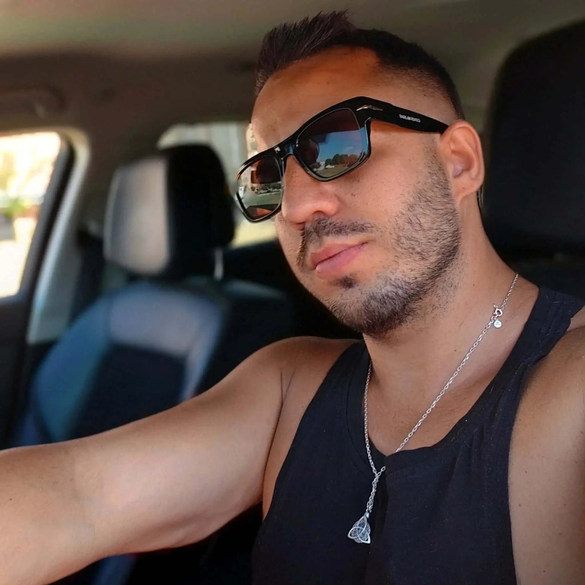 Hombre con gafas de sol retro de montura negra y cristales marrones conduciendo coche, estilo casual y elegante.