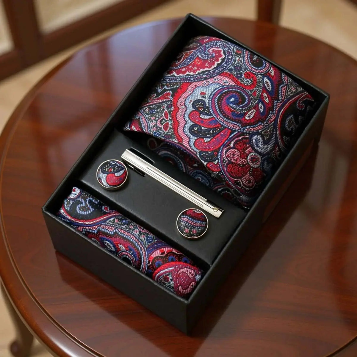 Set de corbata, pañuelo y gemelos con estampado paisley en tonos azul y morado, elegante y detallado en caja de regalo.