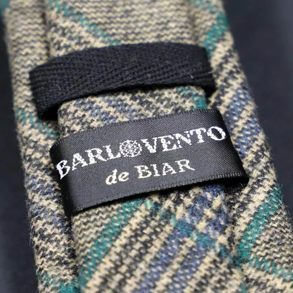 Corbata de lana a cuadros en tonos verde, azul y beige, con textura cálida y etiqueta de marca cosida en el reverso.