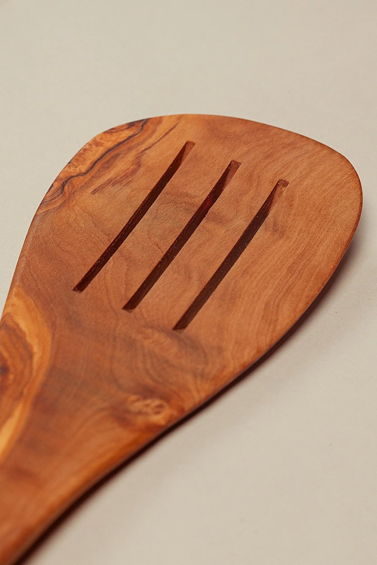 Espátula de madera de olivo con diseño pulido y ranuras, color marrón natural, ideal para cocinar.