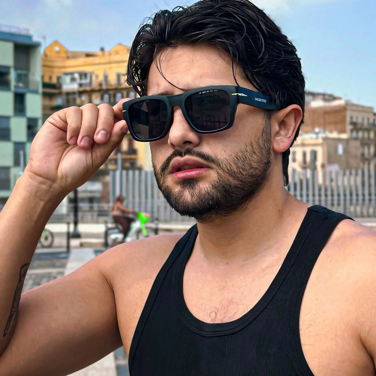 Hombre con camiseta negra y gafas de sol cuadradas de pasta negra con detalles metálicos y protección UV urbana.