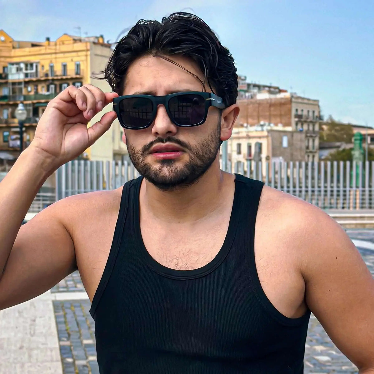 Hombre con camiseta de tirantes y gafas de sol cuadradas negras con detalle metálico y protección UV400 en la ciudad.