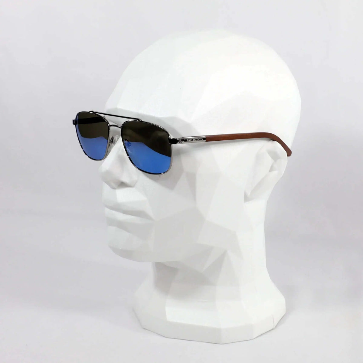 Gafas de sol estilo aviador con lentes azules reflectantes, montura metálica y patillas de madera sobre maniquí blanco.