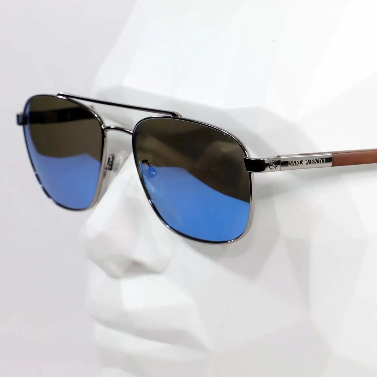 Gafas de sol estilo aviador con montura metálica, lentes azules espejadas y patillas de madera en maniquí blanco.