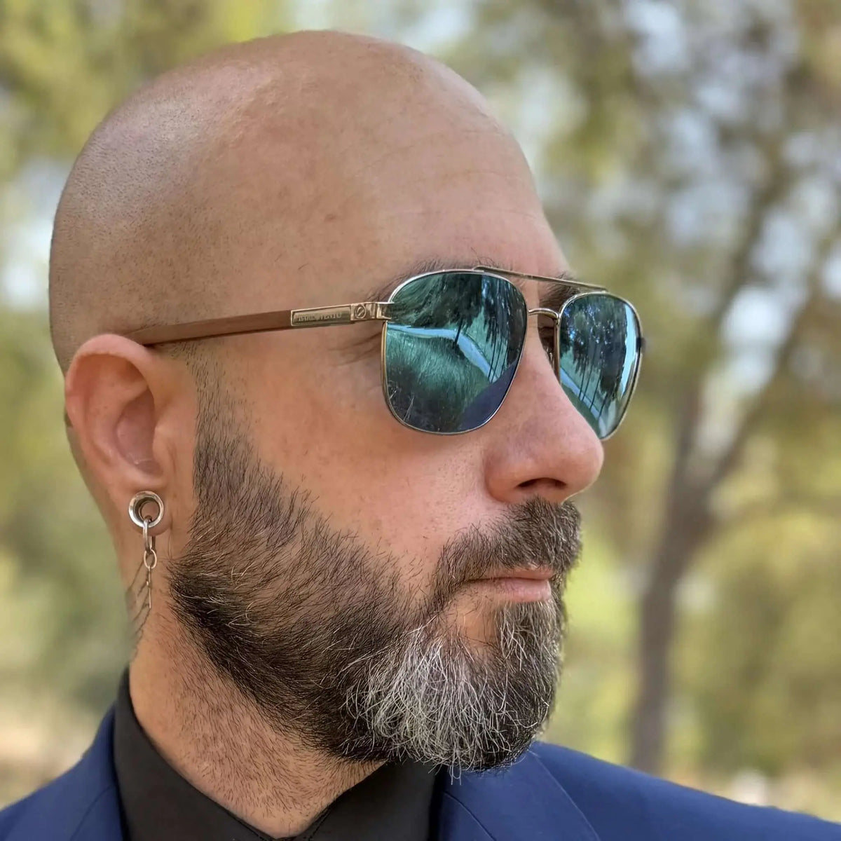 Hombre con gafas de sol tipo aviador, lentes azules espejadas y patillas de madera grabadas, estilo elegante y moderno.