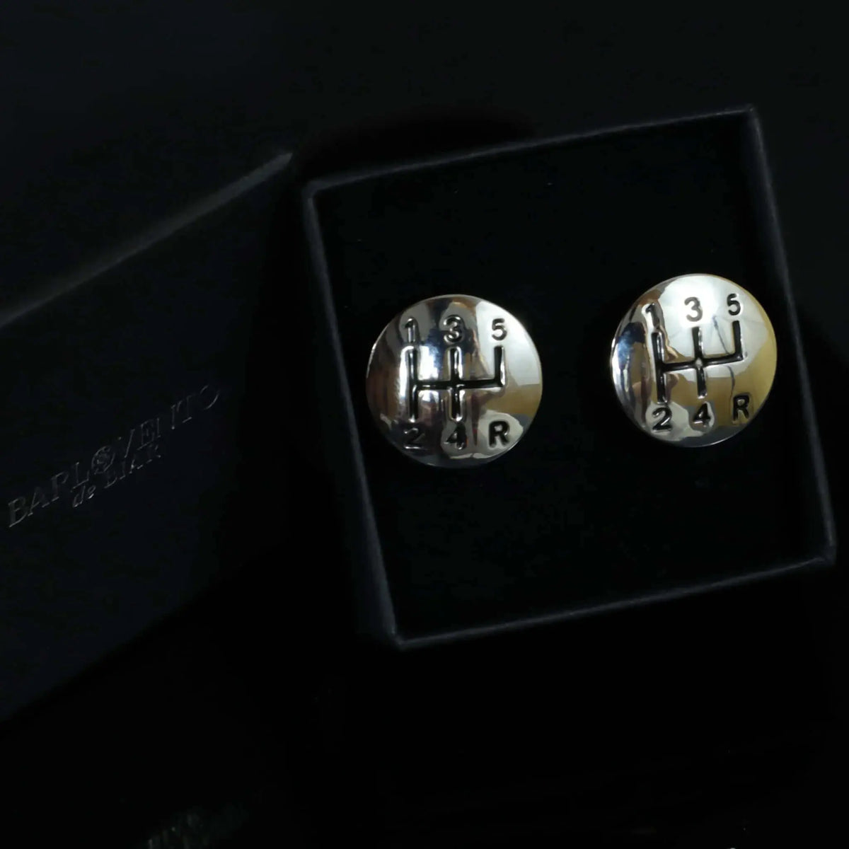 Gemelos de plata redondos con diseño de palanca de cambios manual, acabado brillante, en caja de regalo negra.