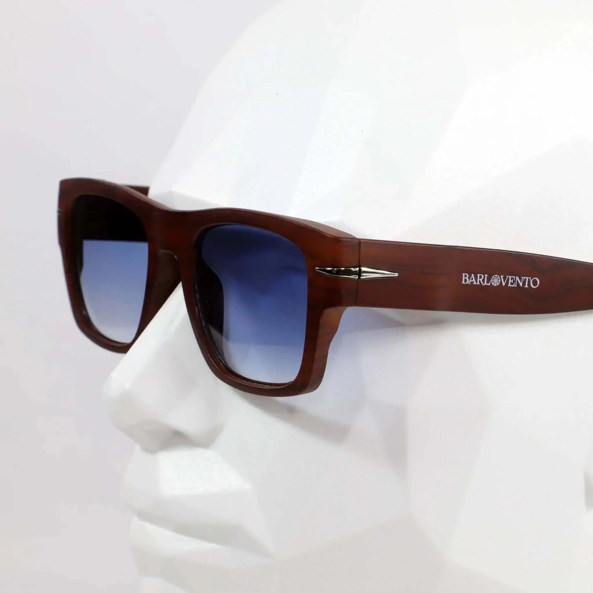 Gafas de sol cuadradas con montura estilo madera marrón y lentes degradadas azules puestas en un maniquí blanco.