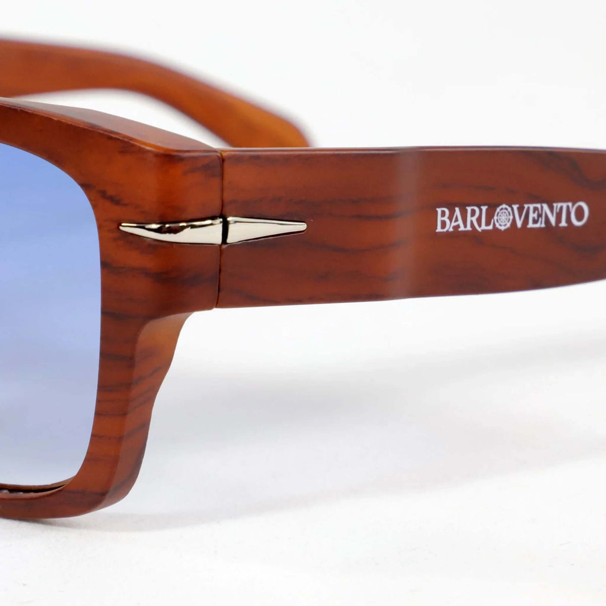 Gafas de sol cuadradas con montura estilo madera marrón, detalle metálico lateral y lentes en tono azul claro.