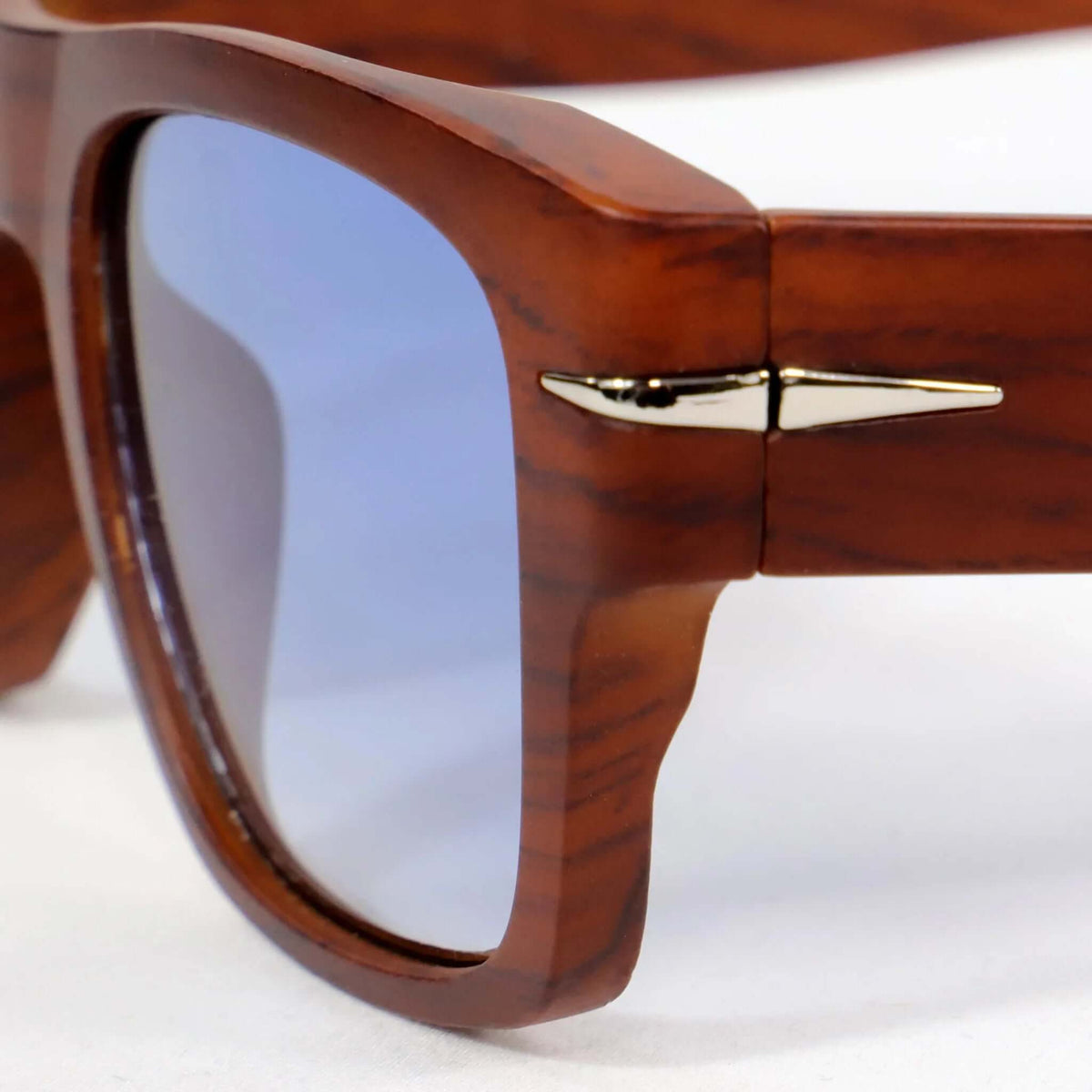 Gafas de sol cuadradas con montura efecto madera marrón y lentes azules, con detalle metálico en la patilla.