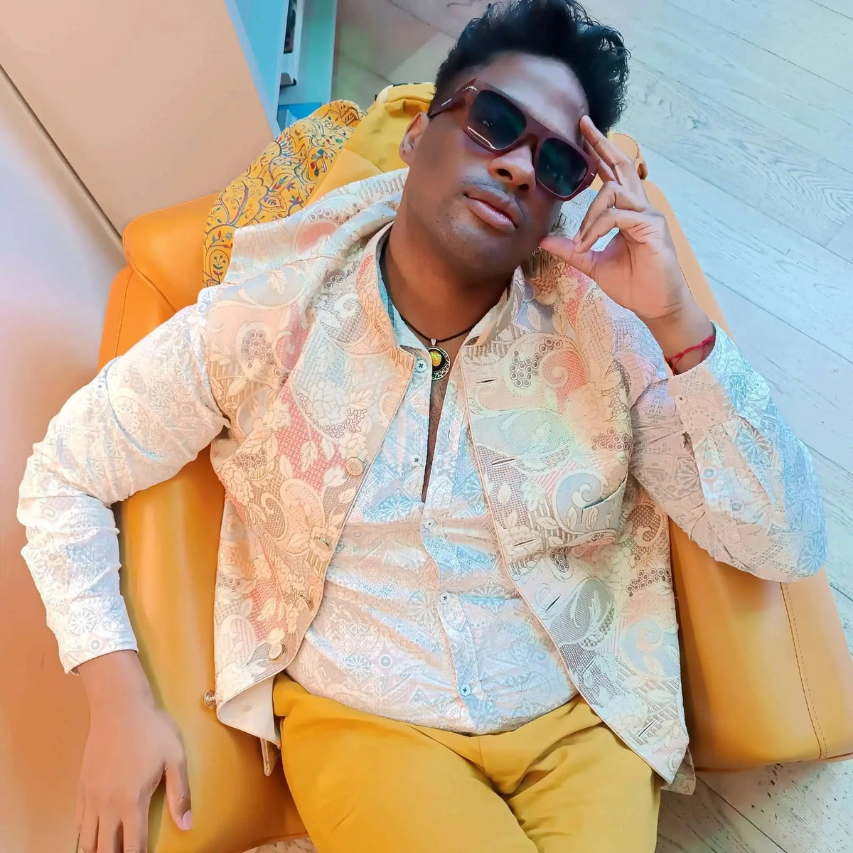 Hombre con gafas de sol cuadradas de madera y lentes azules sentado en un sillón amarillo. Estilo elegante y moderno.