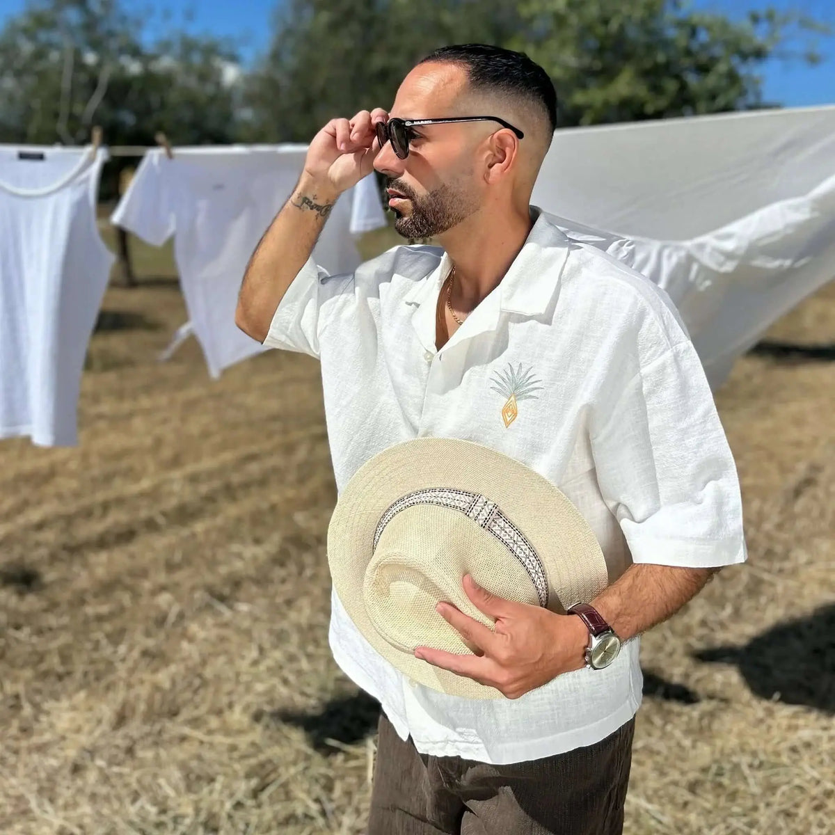 Hombre con camisa blanca y gafas de sol negras de montura clásica y lentes polarizadas verdes en un campo soleado.