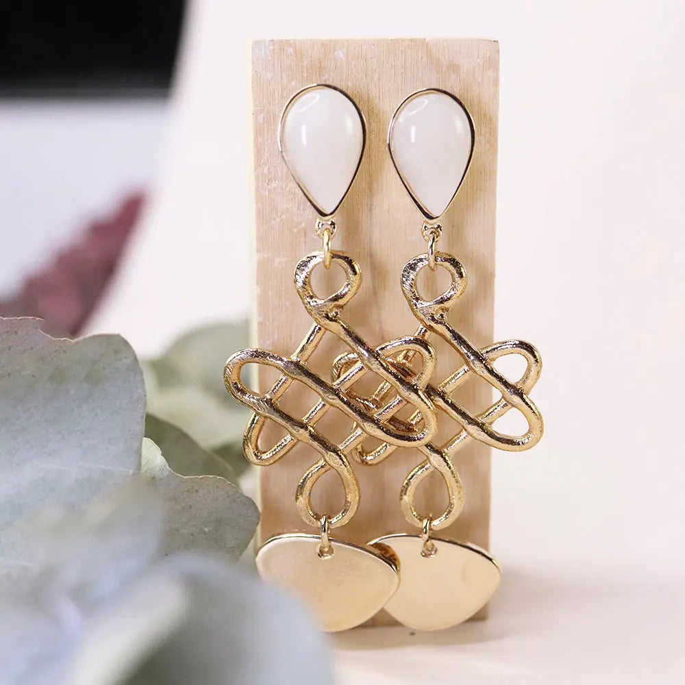 Pendientes dorados con forma de lazo y detalles en acrílico blanco, elegantes y modernos.