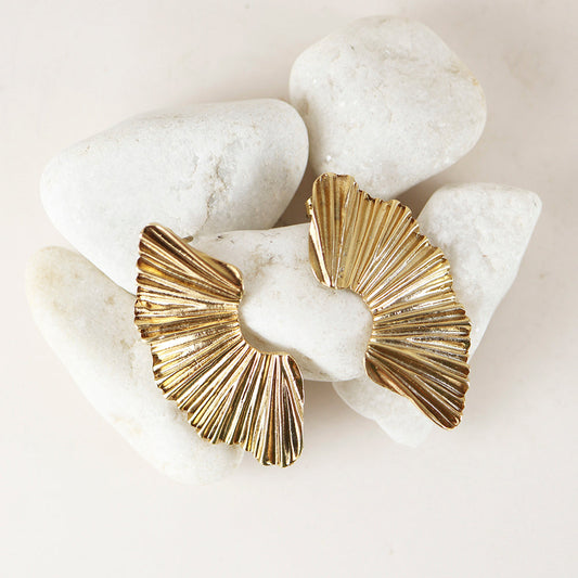 Pendientes de metal dorado con diseño plisado, estilo moderno, sobre fondo de piedras blancas.