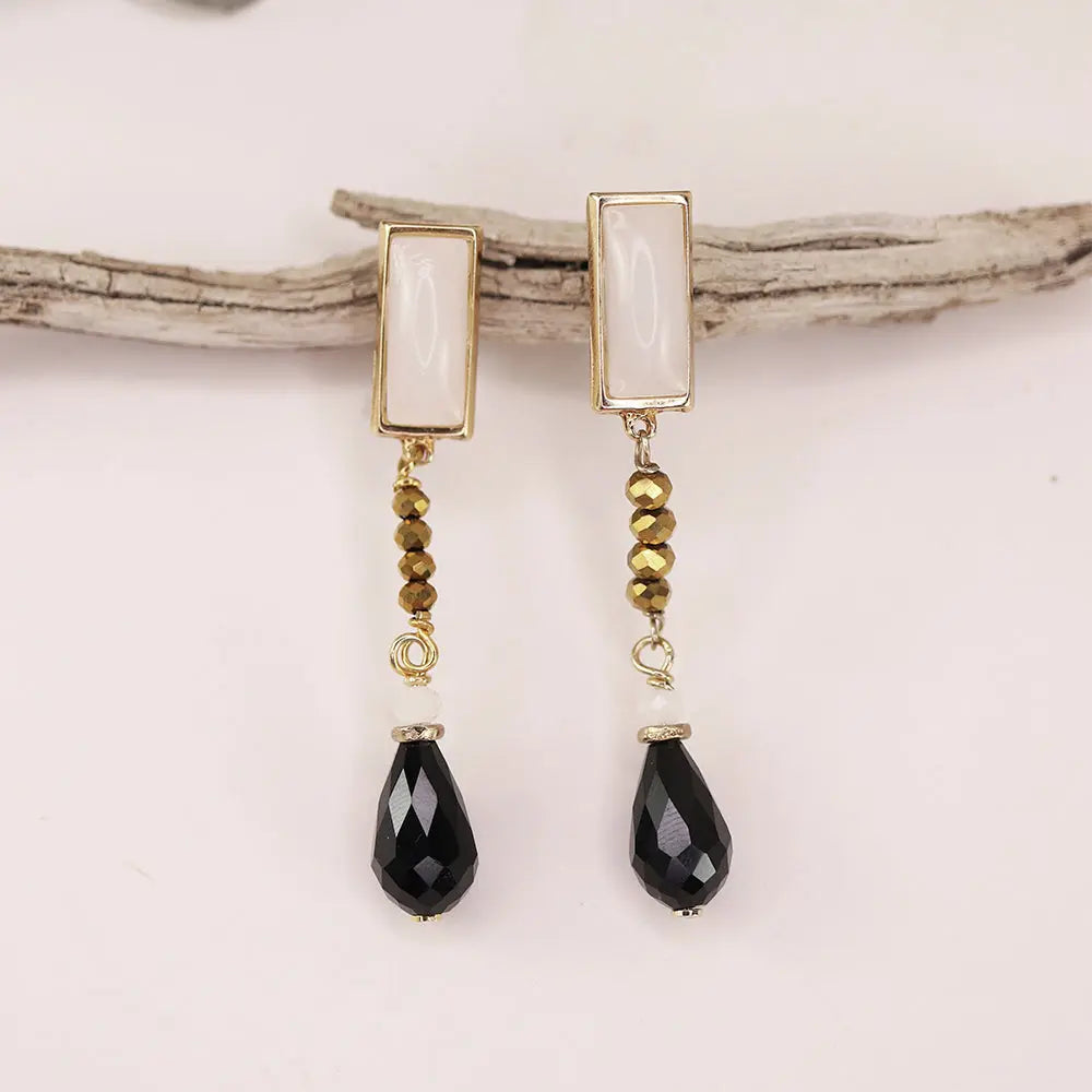Pendientes largos de oro, con cristales marrones y gotas de cristal negro, estilo elegante y moderno.