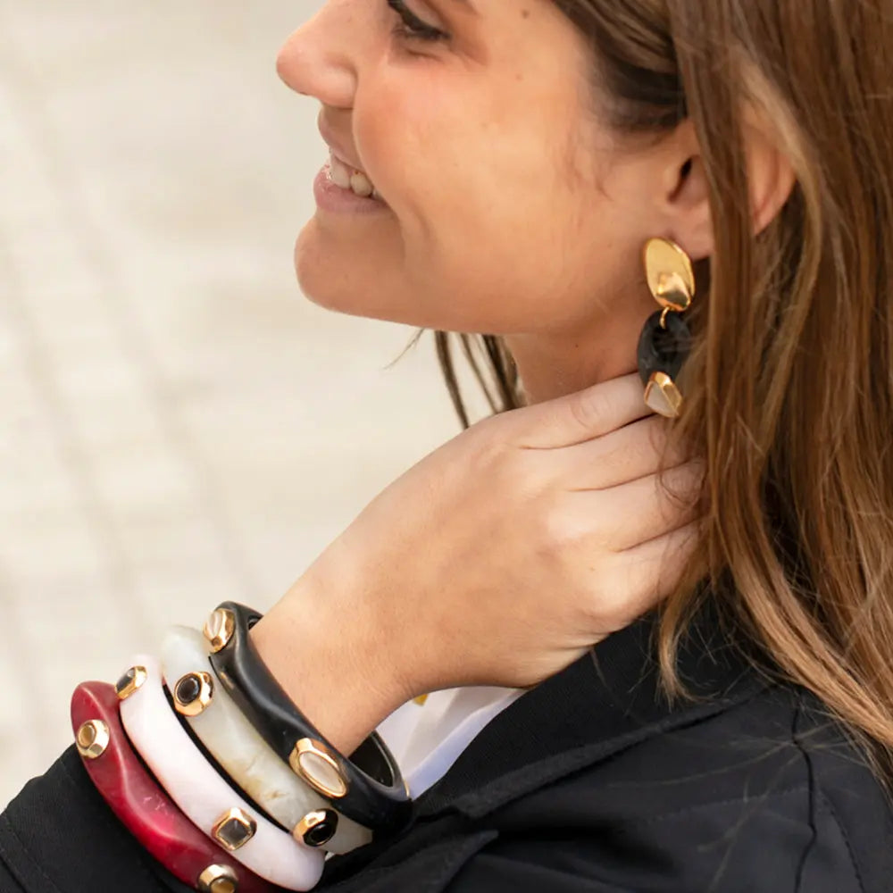 Pulseras de acrílico en rojo, blanco y negro con detalles dorados, y aretes elegantes a juego.