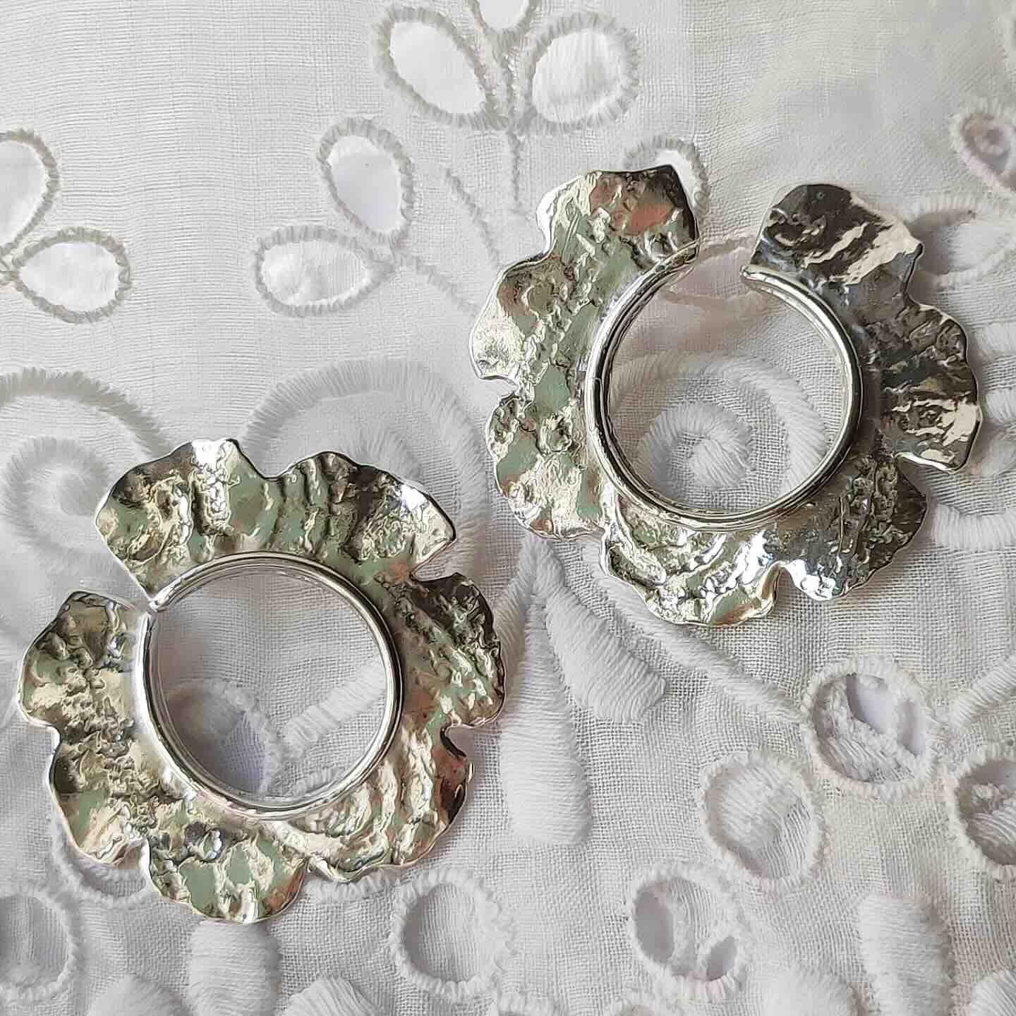 Pendientes de metal plateado con diseño de flor, acabado texturizado, estilo elegante y moderno.