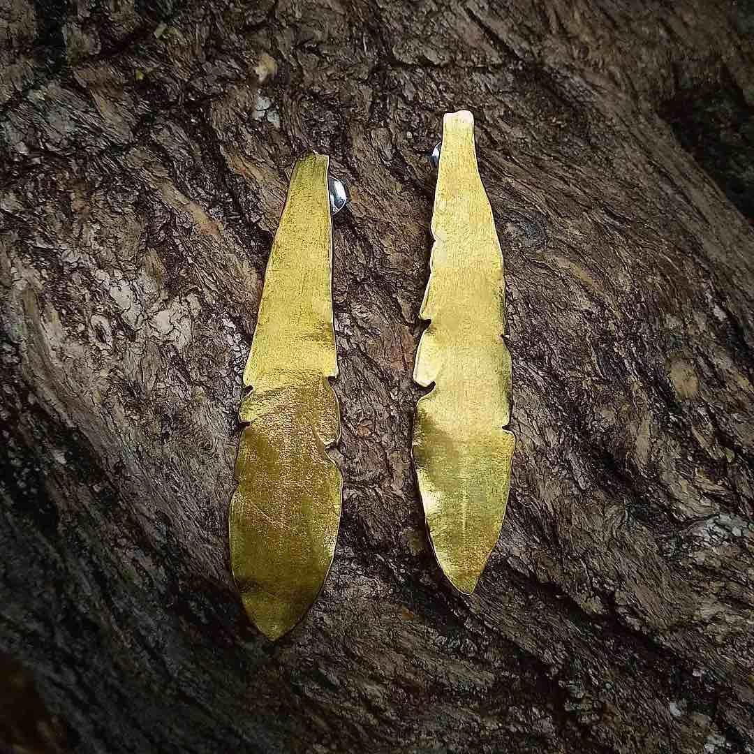 Pendientes largos de metal dorado en forma de pluma, elegantes y modernos, ideales para cualquier ocasión.