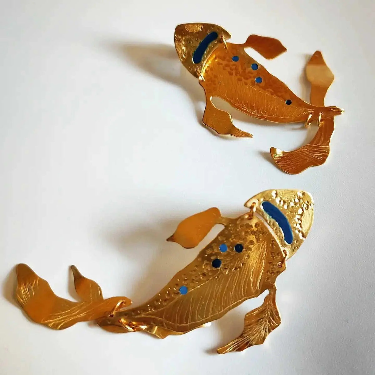 Pendientes de pez koi dorados, detalle en azul y negro, diseño elegante y artístico en metal.