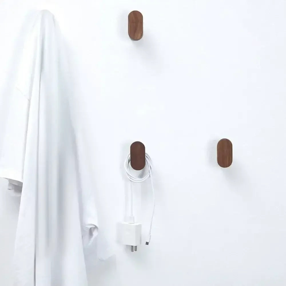 Tres perchas ovaladas de madera maciza en pared blanca. Una sostiene una prenda blanca y otra un cable con cargador.