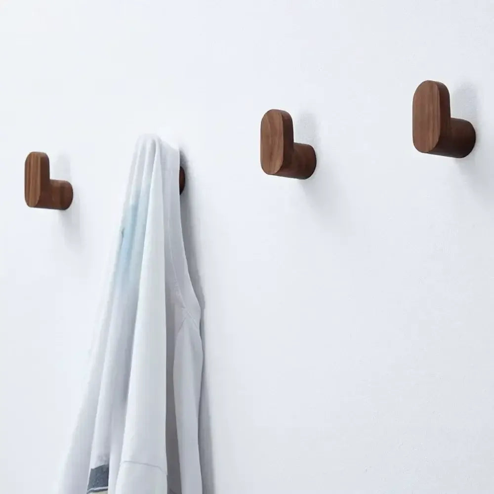 Perchas de pared minimalistas en madera oscura con forma de L, instaladas en una pared blanca, con una prenda colgada.