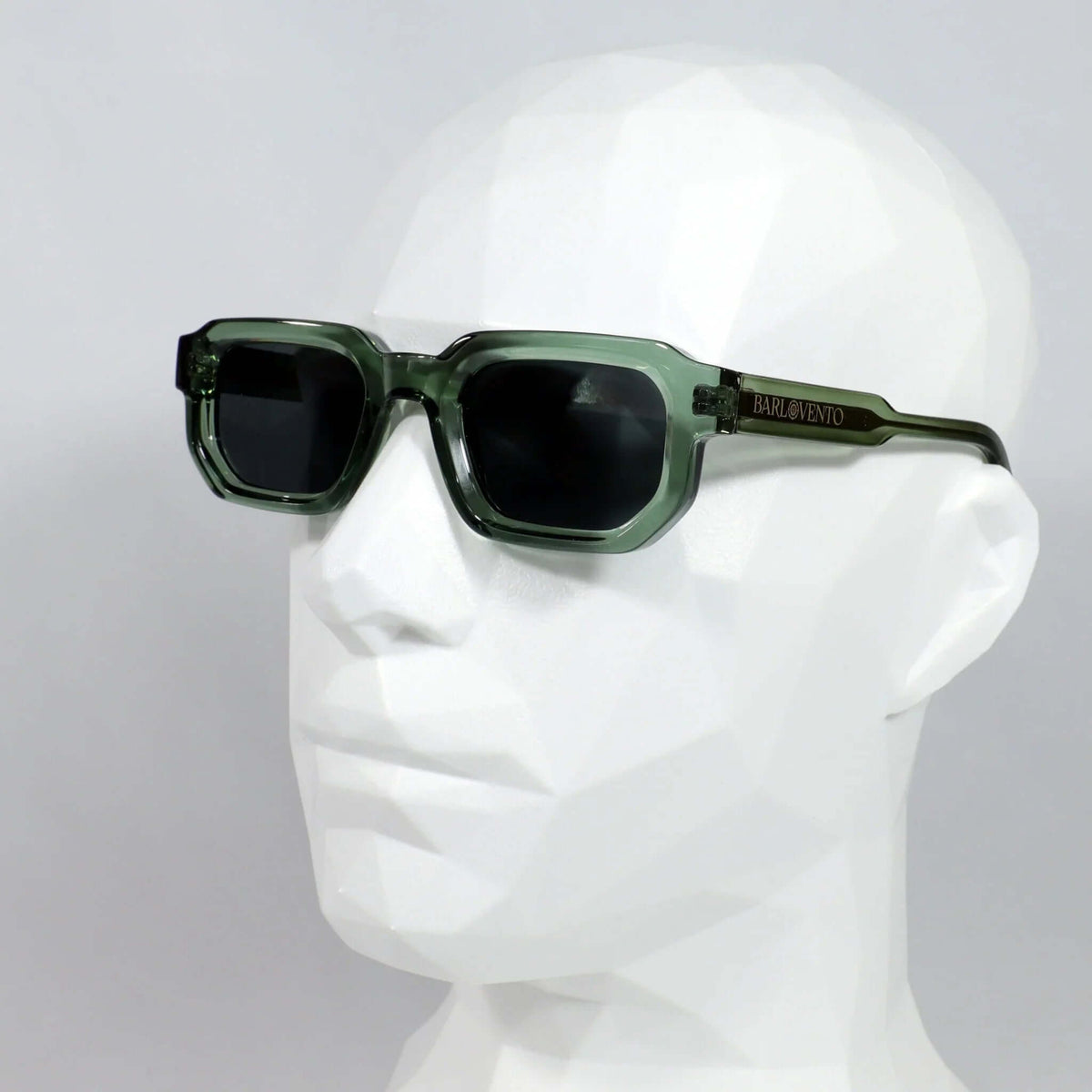 Gafas de sol rectangulares con montura de acetato verde translúcido y lentes oscuras, sobre maniquí blanco.