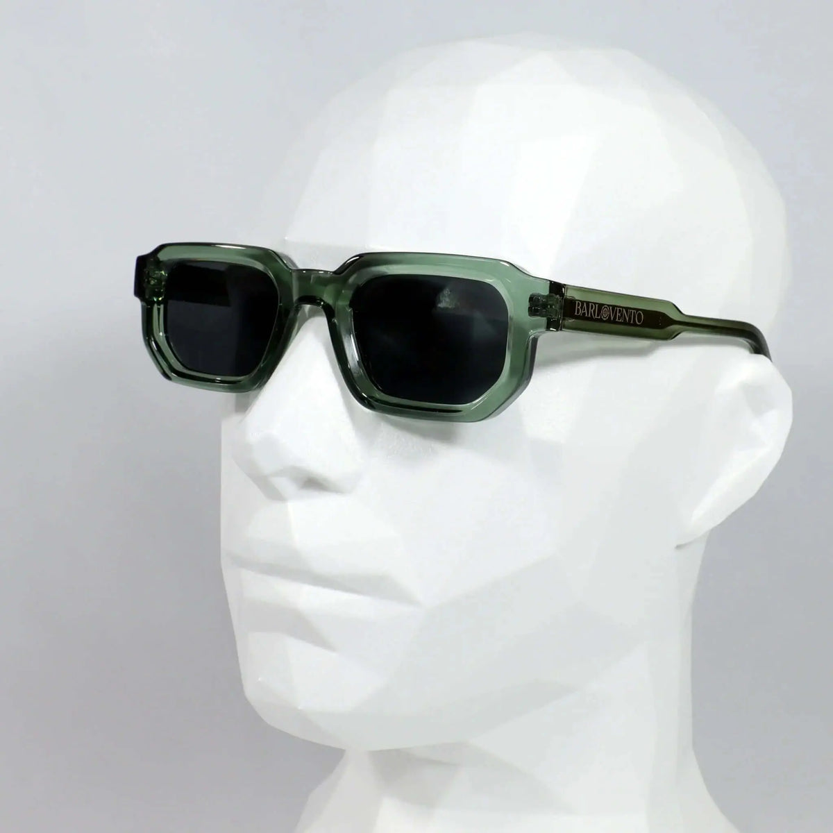 Gafas de sol rectangulares con montura de acetato verde translúcido y lentes oscuras, sobre maniquí blanco.