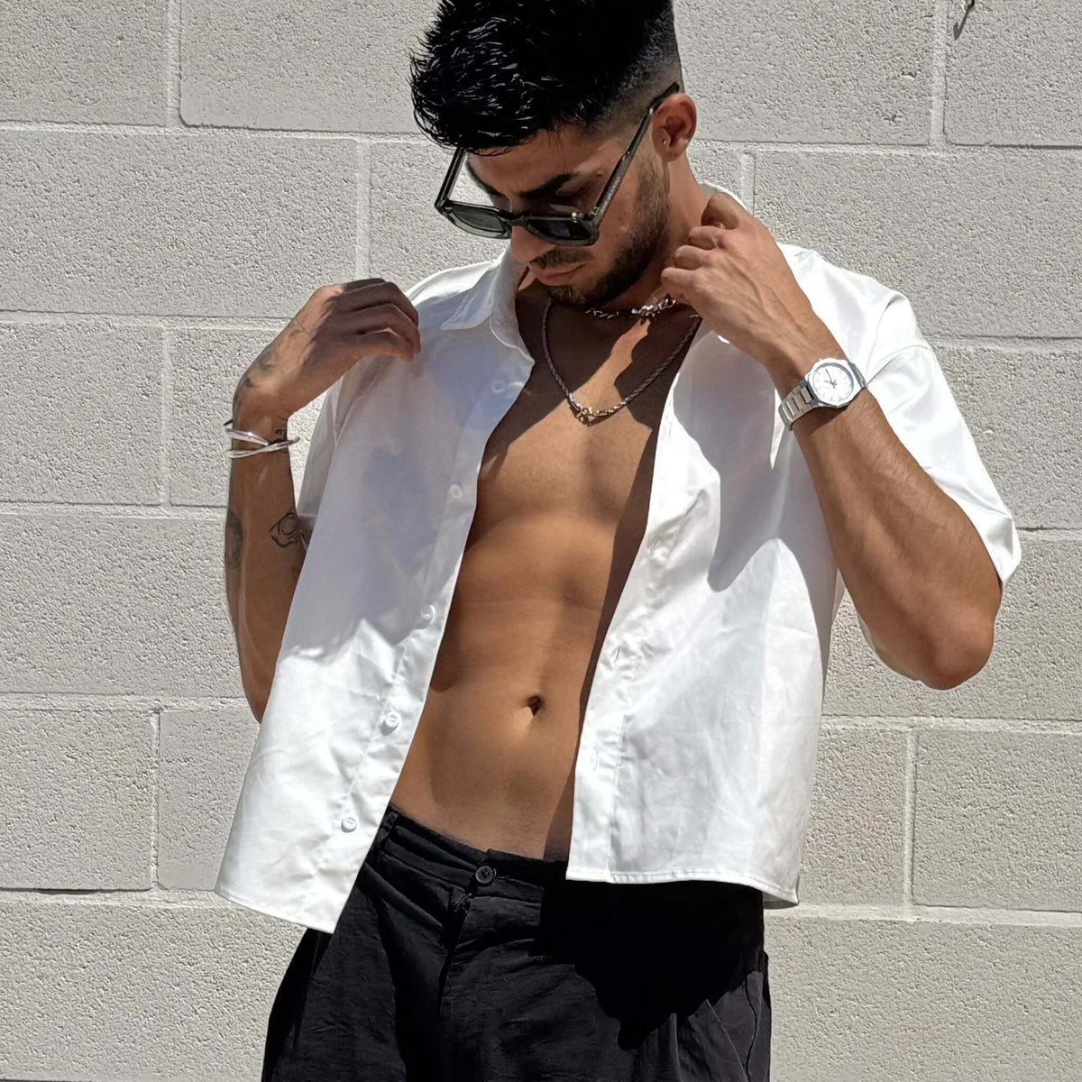 Gafas de sol rectangulares con montura verde y lentes negras, estilo moderno y urbano sobre hombre con camisa abierta.