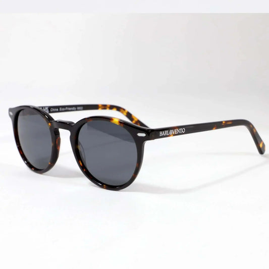 Gafas de sol unisex con montura redonda de carey y lentes oscuras polarizadas sobre fondo blanco. Estilo vintage casual.