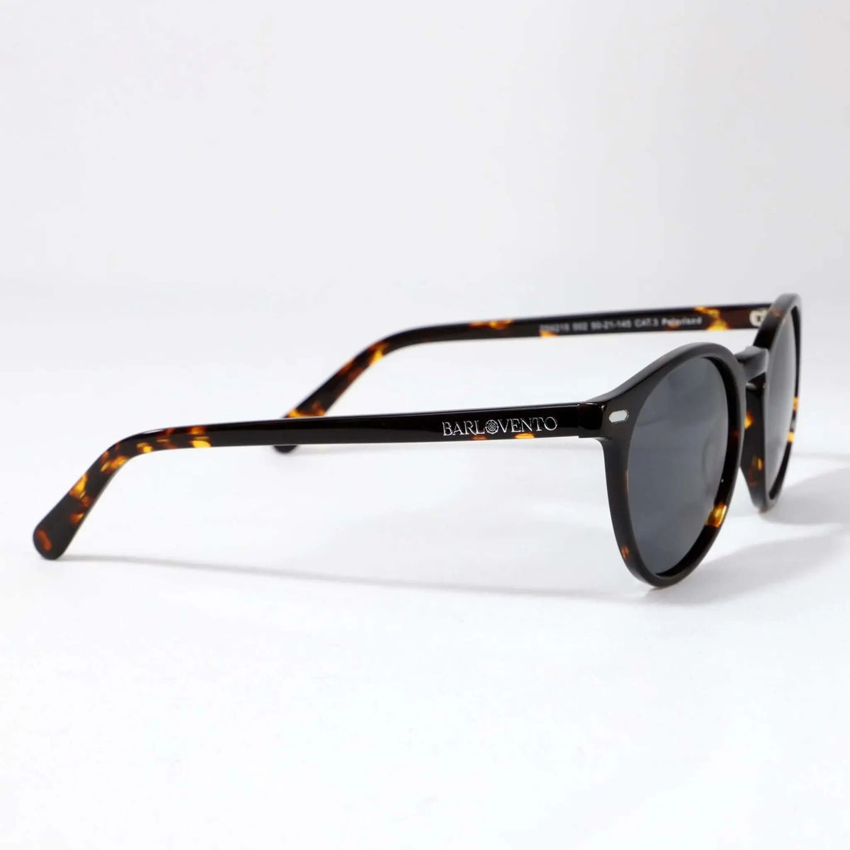 Gafas de sol unisex con montura redonda de carey y lentes polarizadas oscuras sobre fondo blanco. Estilo clásico.