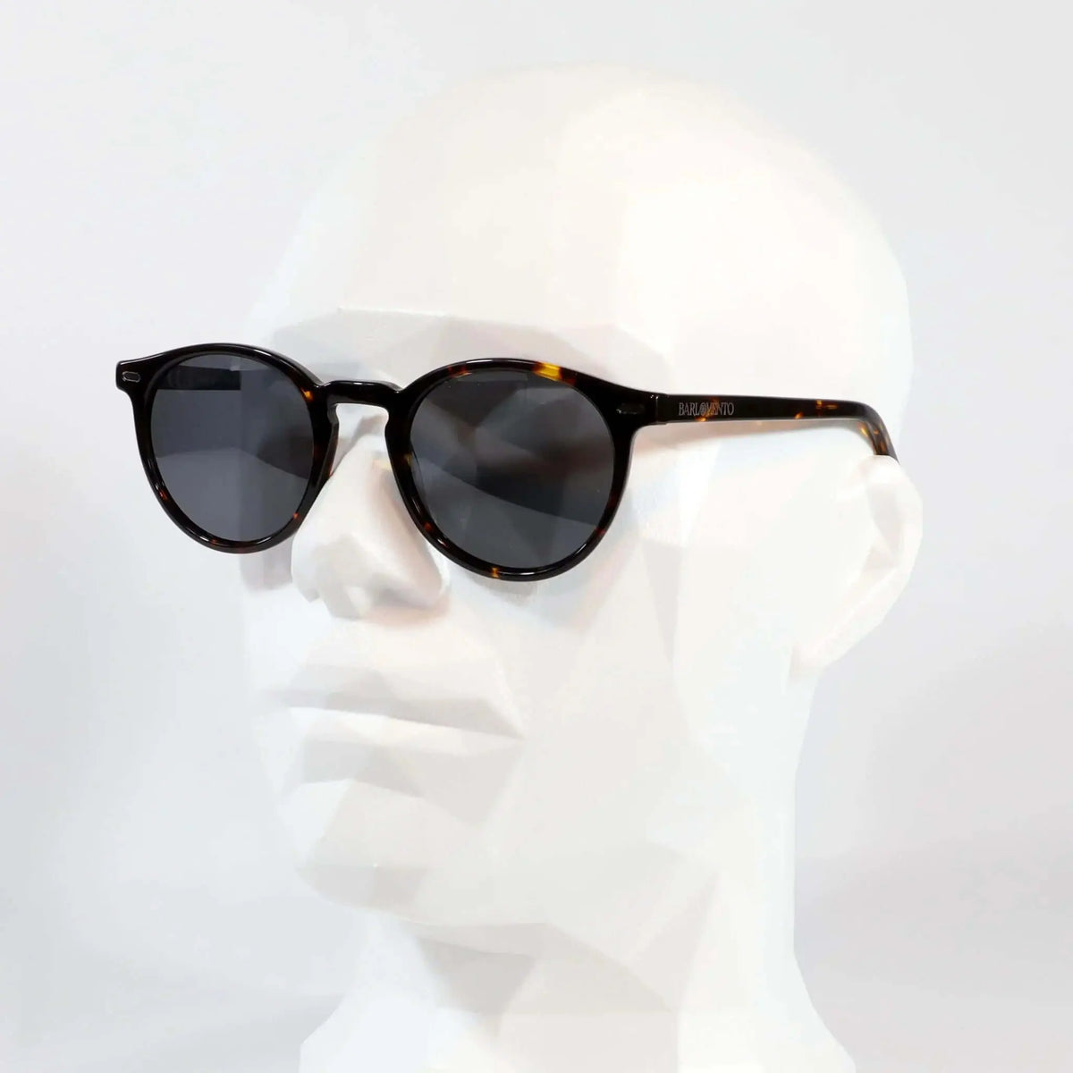 Gafas de sol unisex con montura redonda de carey y lentes polarizadas oscuras sobre maniquí blanco. Estilo clásico.