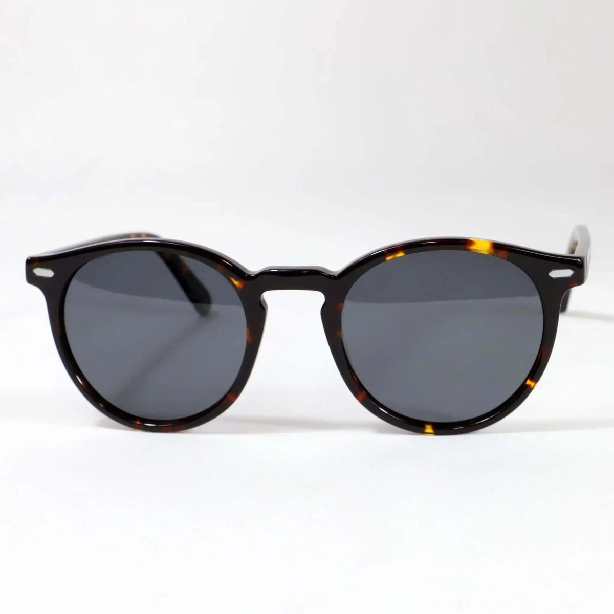 Gafas de sol redondas de carey con montura clásica de acetato y lentes oscuras polarizadas sobre fondo blanco.
