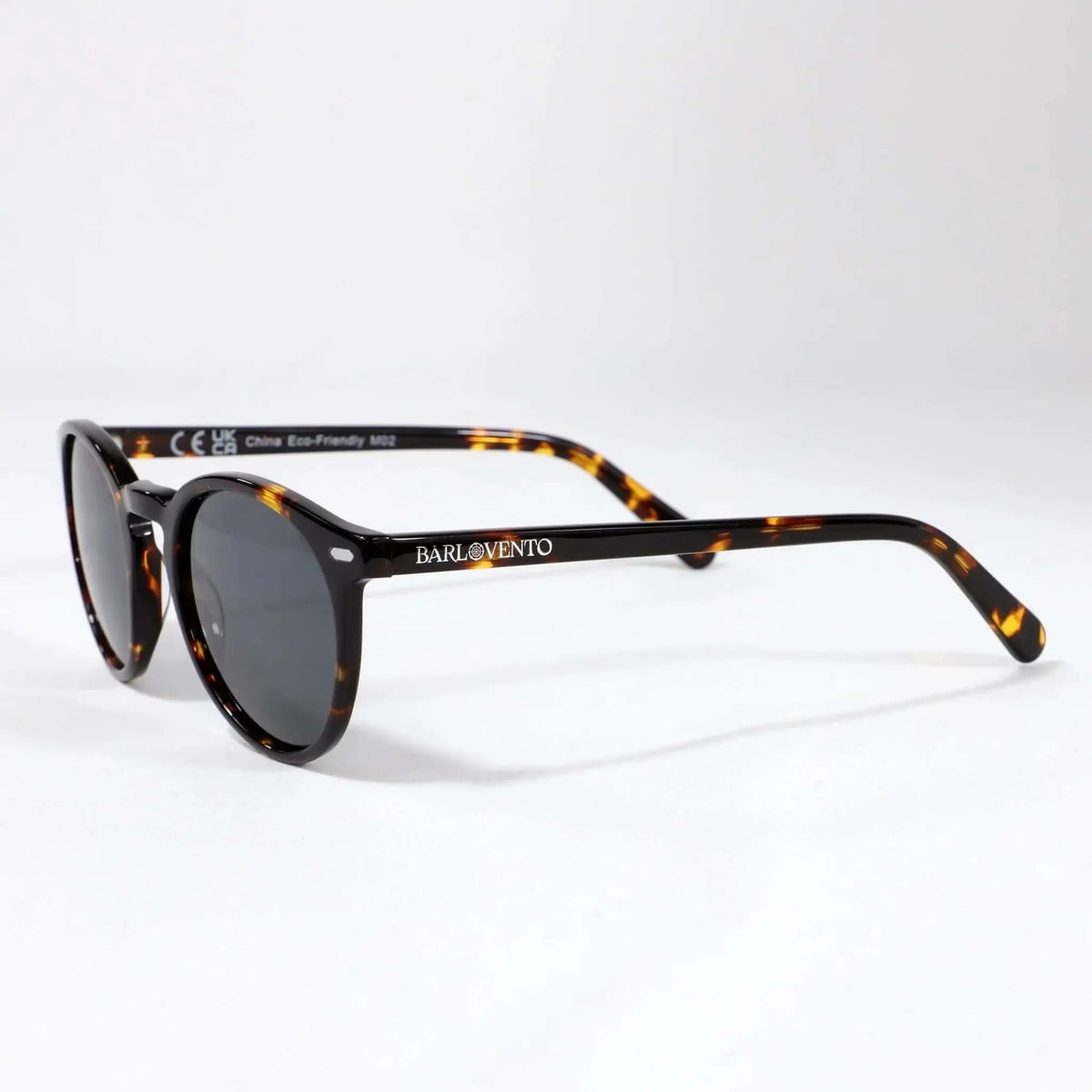Gafas de sol unisex con montura redonda de carey y lentes polarizadas oscuras sobre fondo blanco. Estilo clásico.