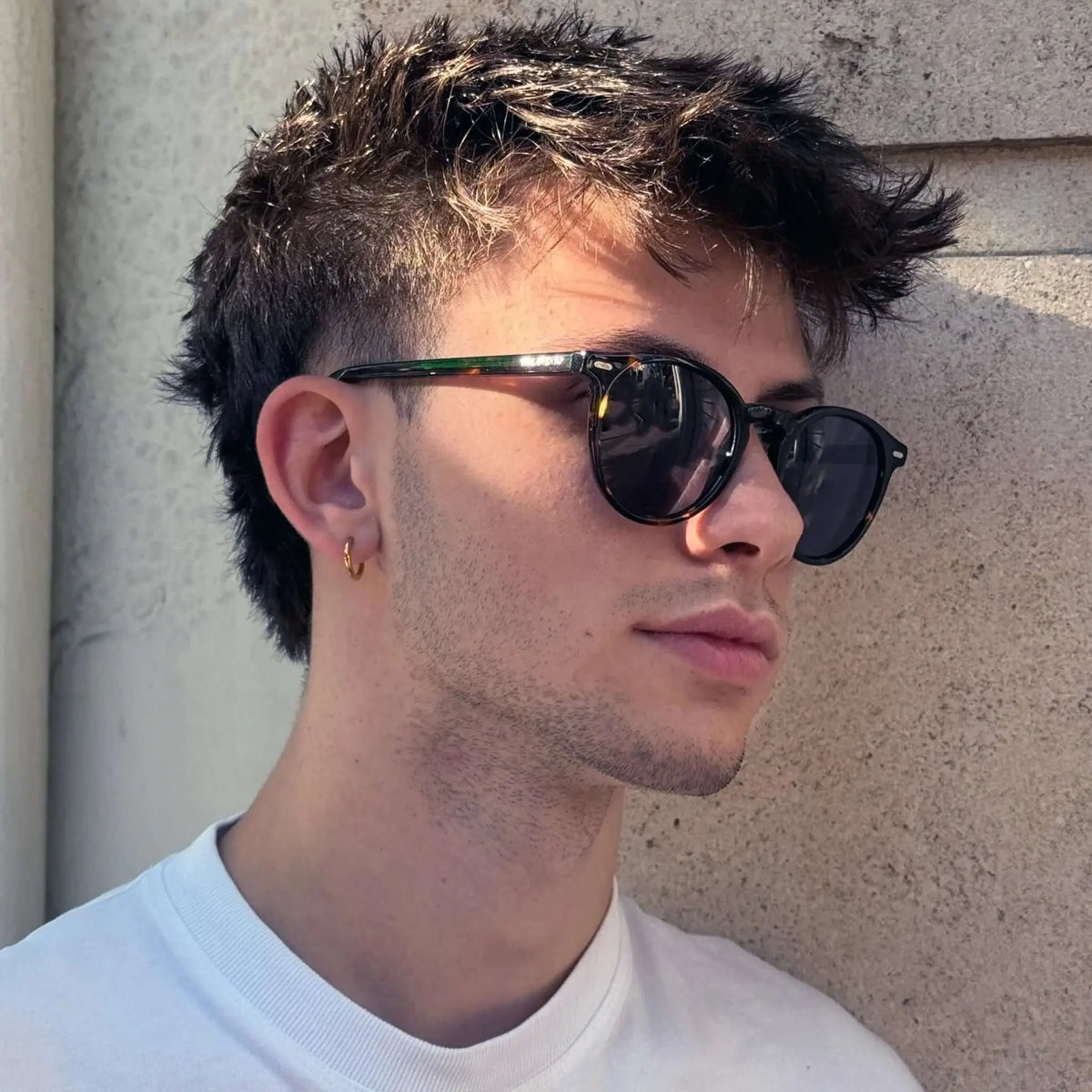 Joven con gafas de sol redondas de carey, montura de acetato y lentes polarizadas marrones estilo clásico y casual.