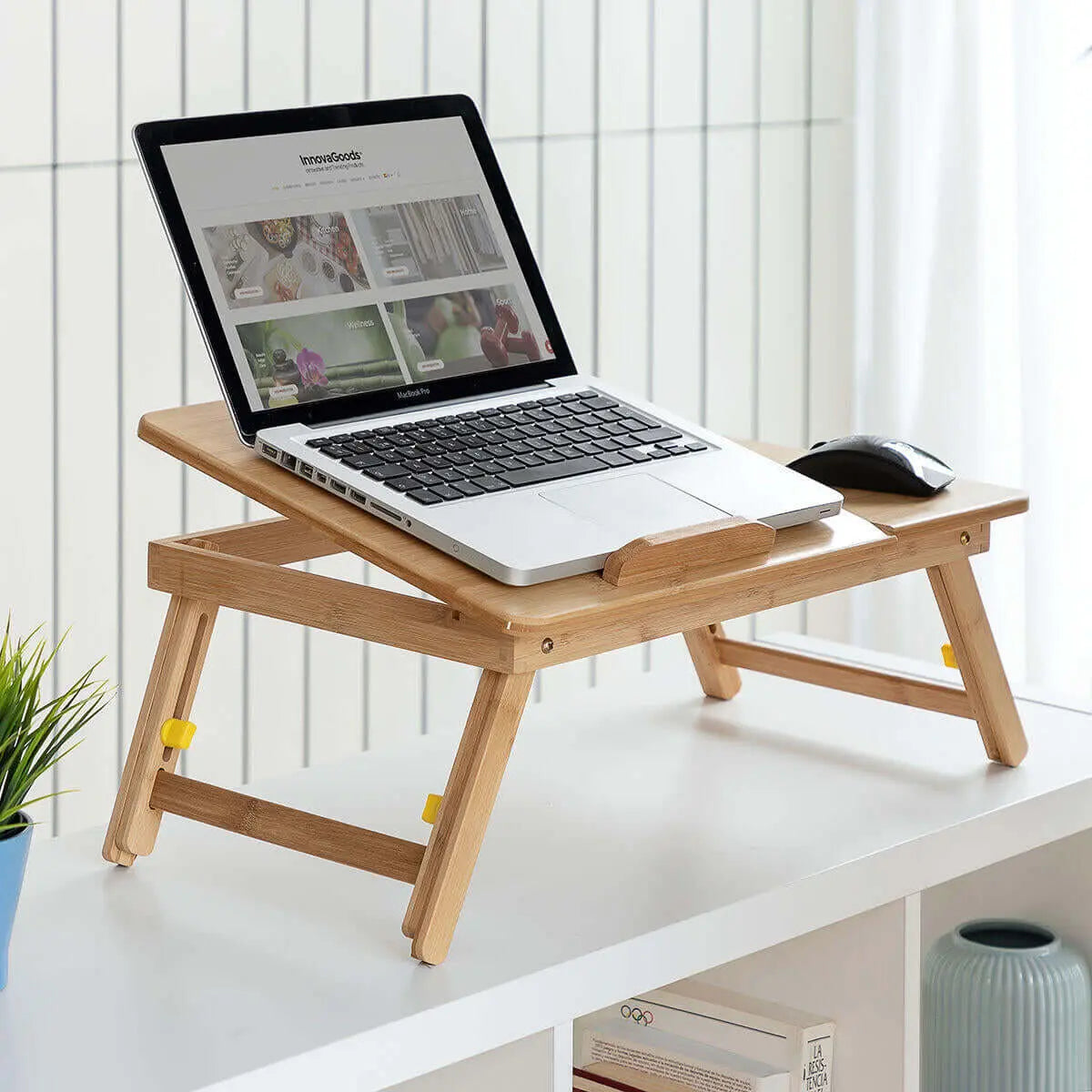 Mesa auxiliar plegable de bambú color madera natural con un ordenador portátil sobre una superficie blanca.