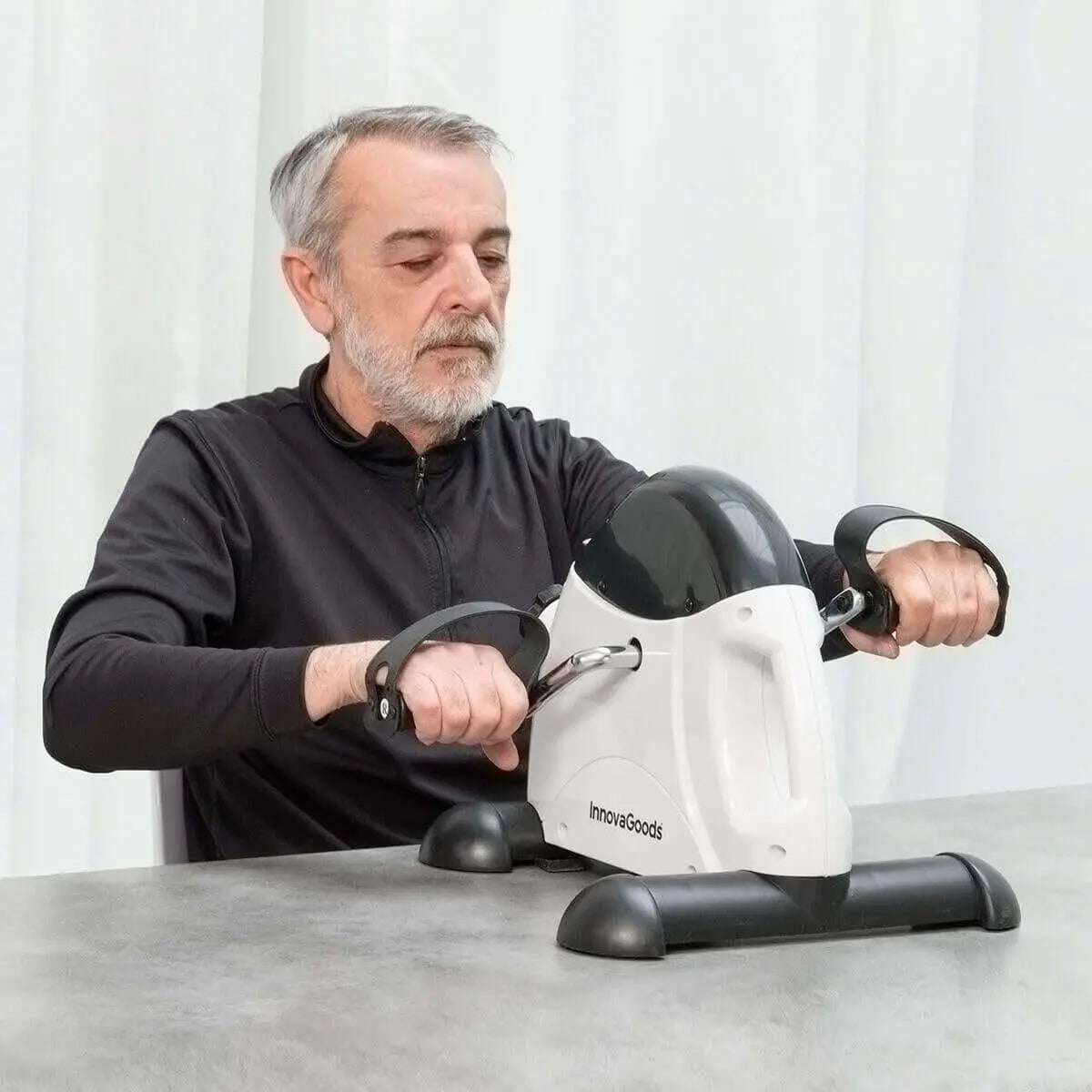 Hombre ejercitando sus brazos con un pedaleador compacto blanco y negro con pantalla digital sobre una mesa.