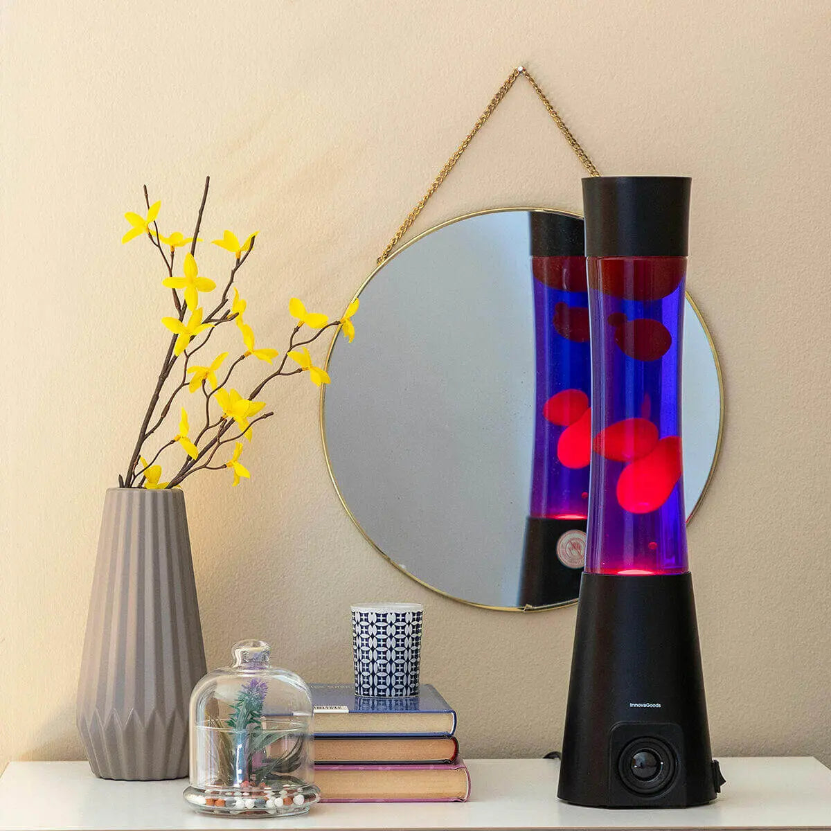 Lámpara de lava con altavoz, cilindro de cristal azul con cera roja, base negra sobre mesa con decoración.