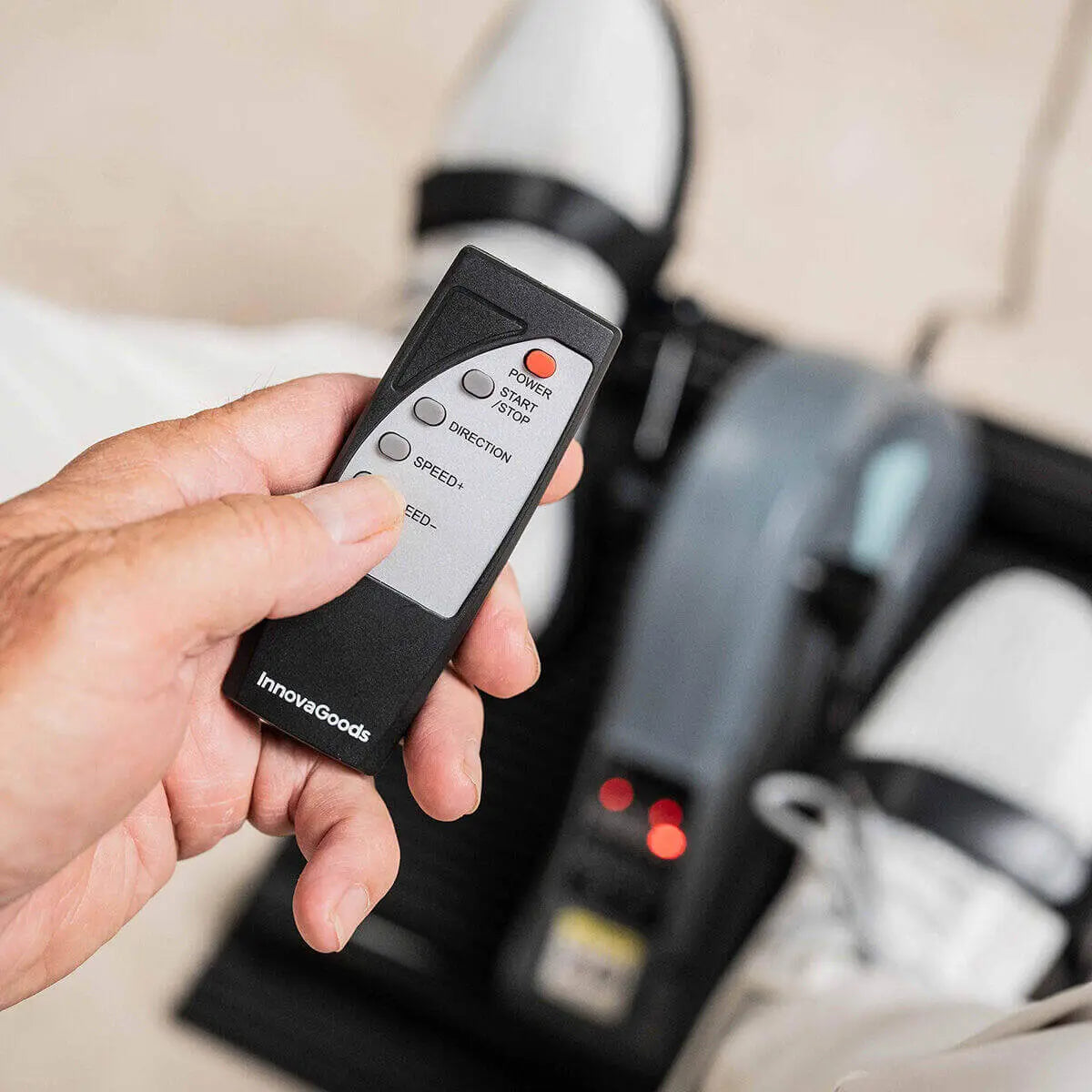 Mano sosteniendo un mando negro de pedaleador eléctrico con botones para ajustar velocidad y dirección del ejercicio.