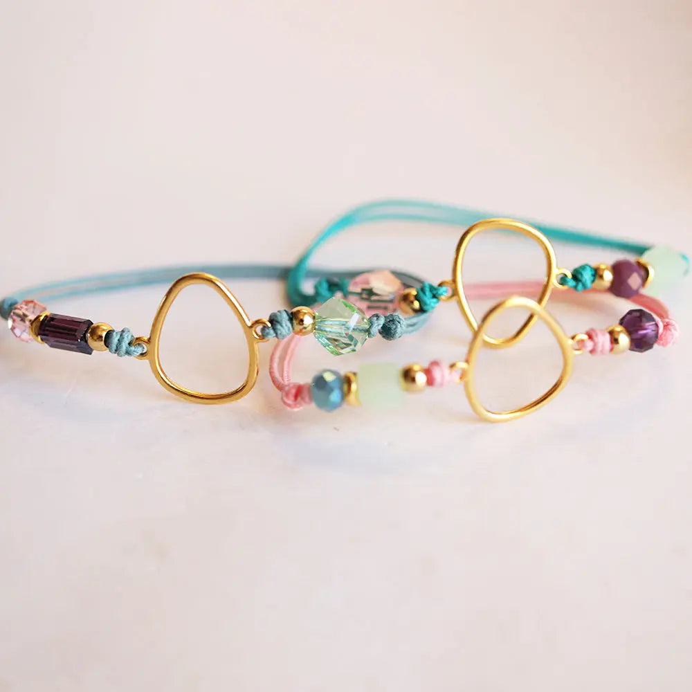 Pulsera de cuentas de cristal en tonos pastel, con detalles dorados y cordones de algodón en azul y rosa.