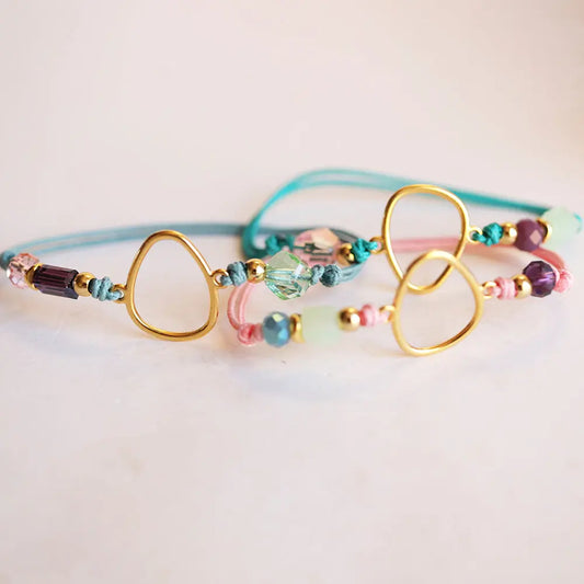 Pulsera de cuentas de cristal en tonos pastel, con detalles dorados y cordones de algodón en azul y rosa.
