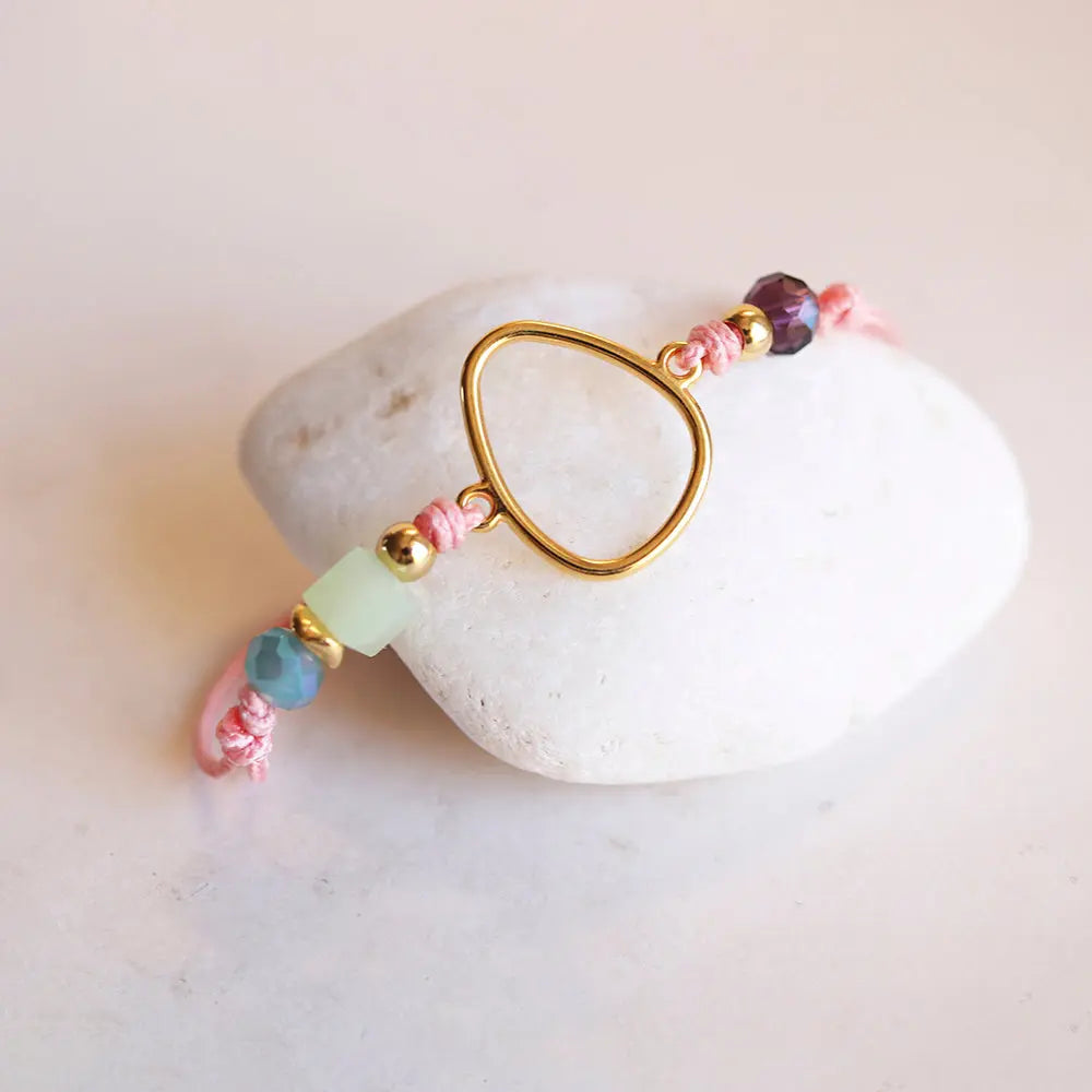 Pulsera artesanal rosa con cuentas de vidrio verde y morado, y detalle dorado en forma de gota.