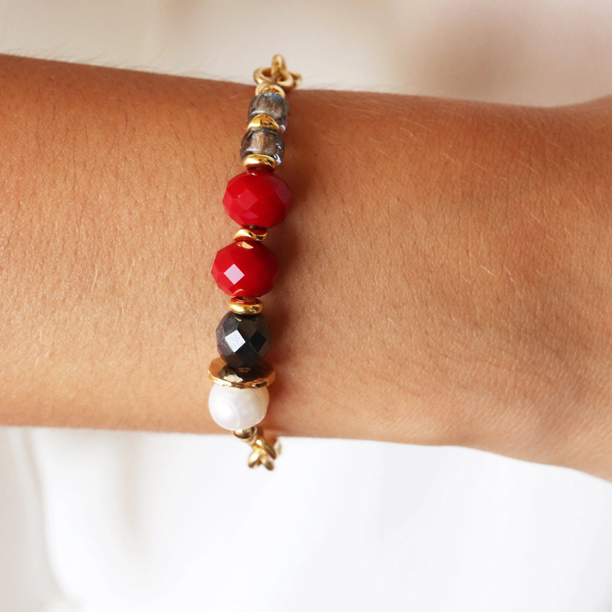 Pulsera de cuentas de cristal rojo, negro y perladas, con detalles dorados, estilo moderno y elegante.