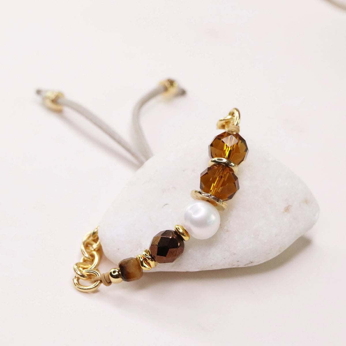 Pulsera elegante con cuentas de cristal ámbar, perla blanca y detalles dorados, sobre fondo de piedra blanca.