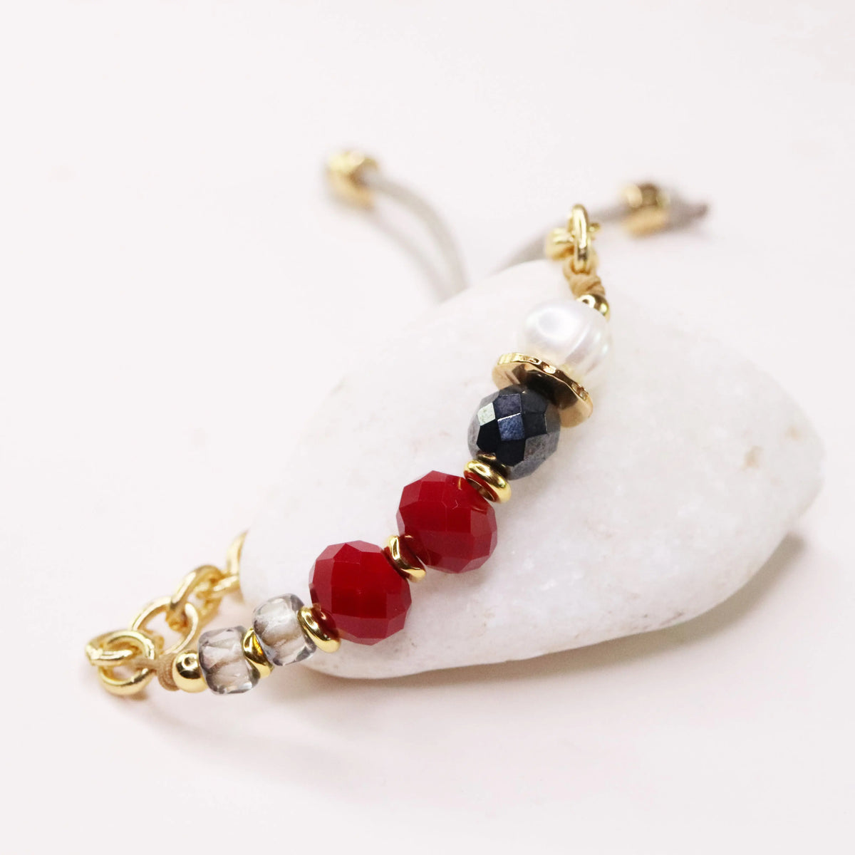 Pulsera de cuentas rojas, negras y perlas con detalles dorados, estilo elegante y moderno.