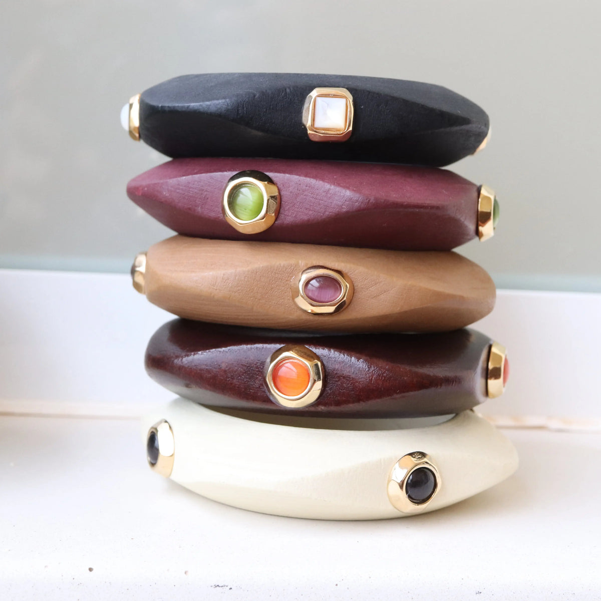 Pulseras de madera en tonos negro, marrón, beige, y burdeos con adornos dorados y piedras de colores.